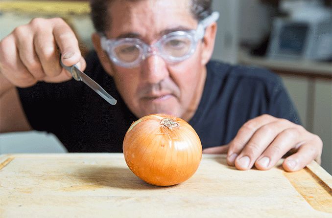 man cutting an onion wearing onion goggles