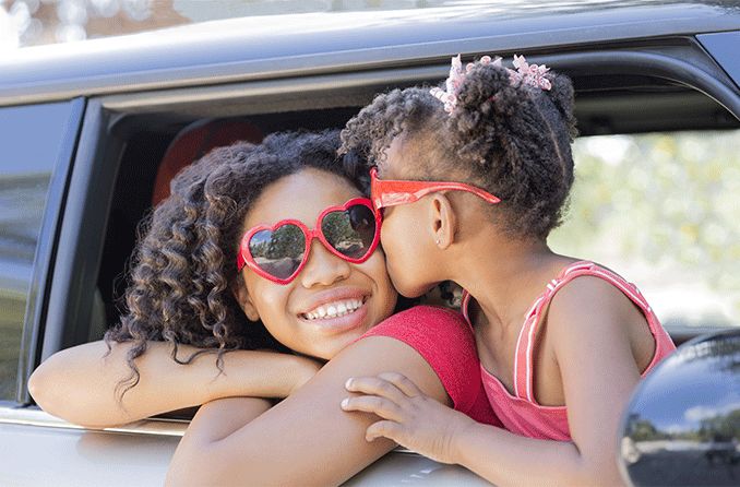 woman leaning outside of a car wearing red heart shaped sunglasses with her daughter