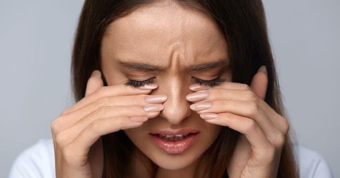 Женщина закрывает глаза пальцами из-за ощущения жжения