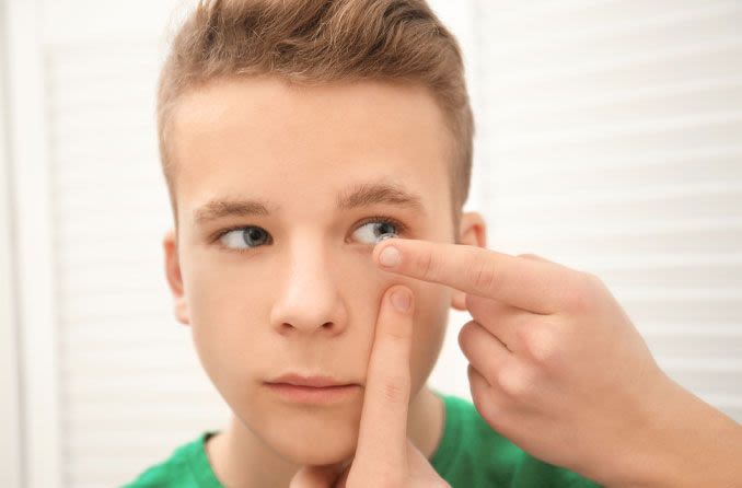 Teen boy inserting contact into eye