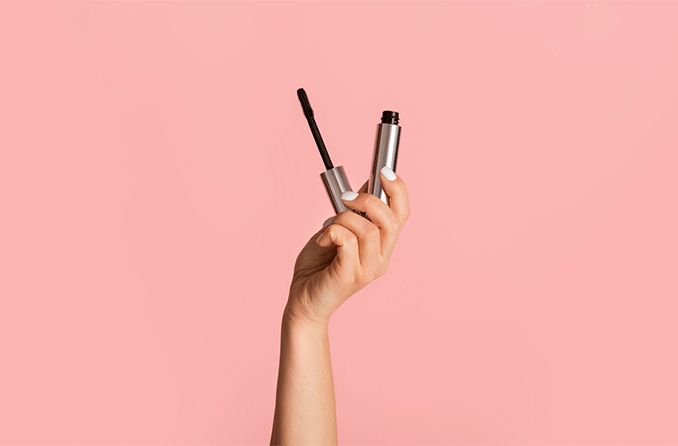 person's hand holding hypoallergenic mascara on pink background