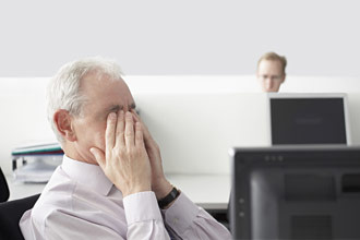 Trabajador de oficina frotándose los ojos mientras está sentado delante de la computadora.
