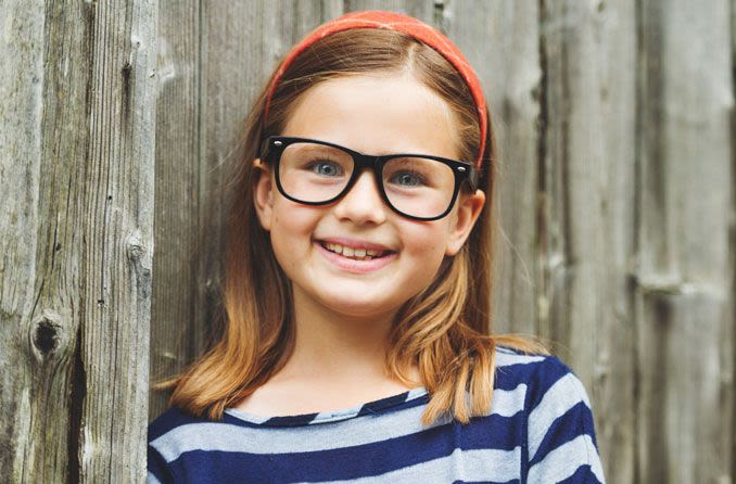 Young girl leaning on fence wearing glasses