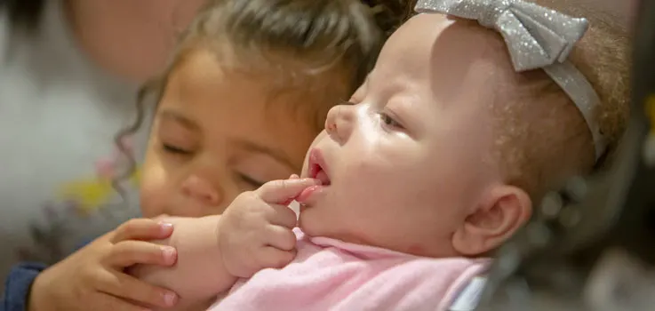 Ramiah Martin sits reclined in a stroller; her sister sits beside her, placing her hand on Ramiah's arm.