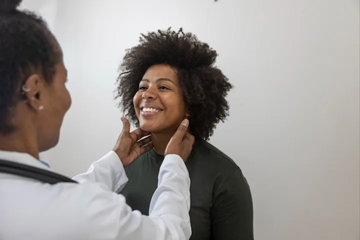 A female doctor feels the sides of the neck of a female patient