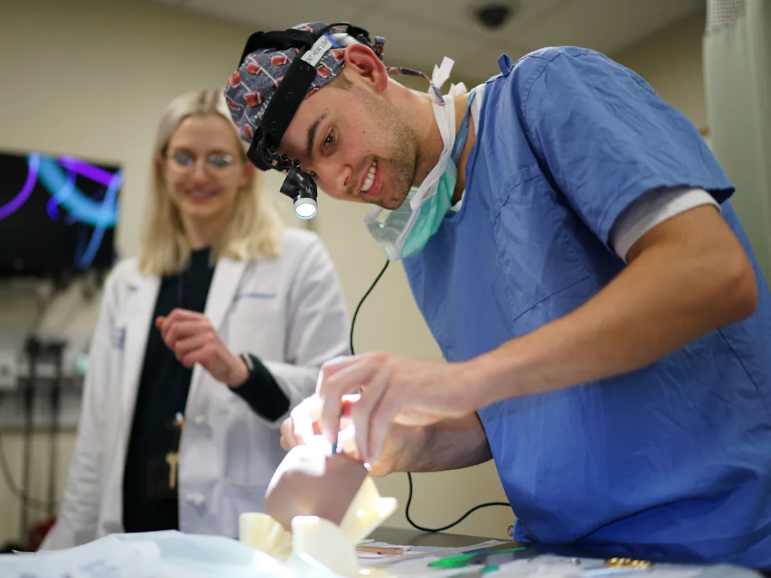 Resident uses a headlight to perform a cleft palate simulation on a training model with guidance from faculty members.