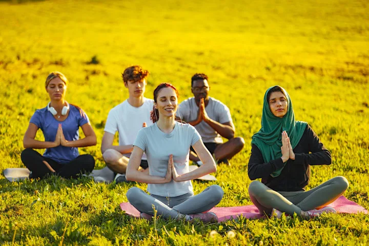 5 people in lotus poses while they practice yoga in a grassy field