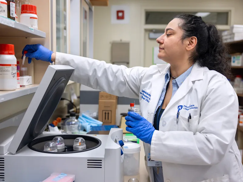 A scientist reaches for a sample on the shelf while preparing a centrifuge in the Neuroscience Institute lab