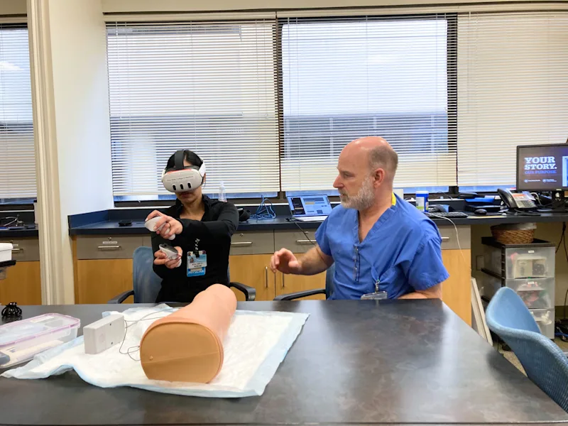 Medical student wearing a VR headset practices IV insertion with guidance from an instructor in the simulation lab