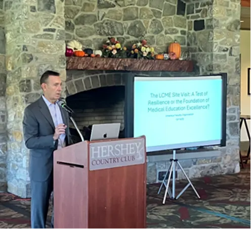 Kevin Black speaks behind a lectern with Hershey Country Club on it and a slide displayed to his left