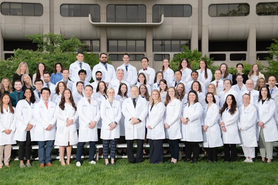 Department of Otolaryngology team members in white coats and professional attire, posed in front of building.