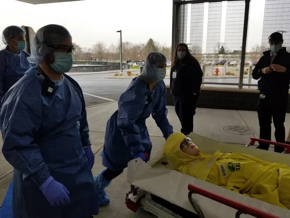 Doctors in full body protective gear wheel a patient on a stretcher during a training exercise.