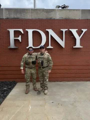 Two fellows wearing tactical gear in front of a wall with the letters FDNY