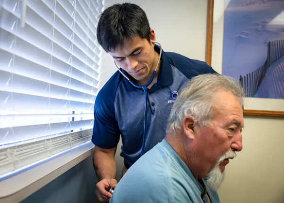 A 3+ program MD student listens with a stethoscope on a patient's back