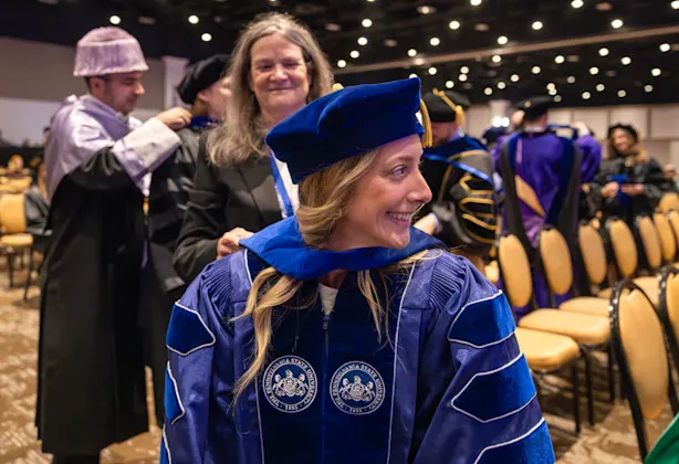 A graduate student smiles and looks off to her left while being hooded