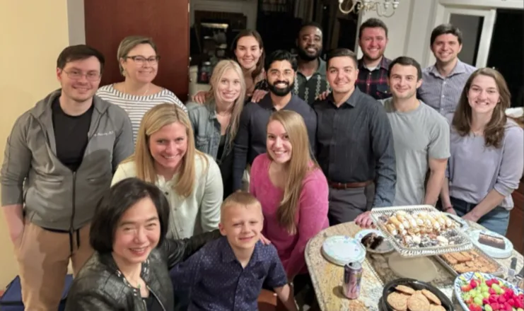 A group of about 15 people in a home near a table with baked goods on it