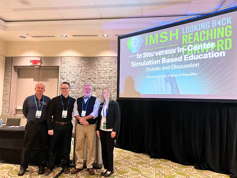 Group of four presenters standing in front of an IMSH conference screen after a simulation education session.