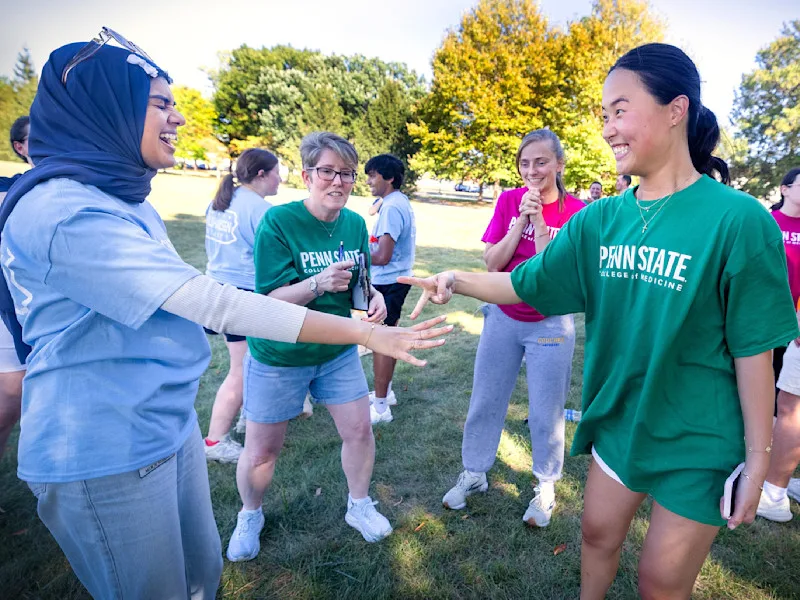 Two MD students laugh while playing rock, paper, scissors with a faculty leader pointing from between them