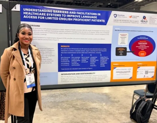 Woman stands next to large poster on healthcare barriers and improving language access to limited English proficient patients