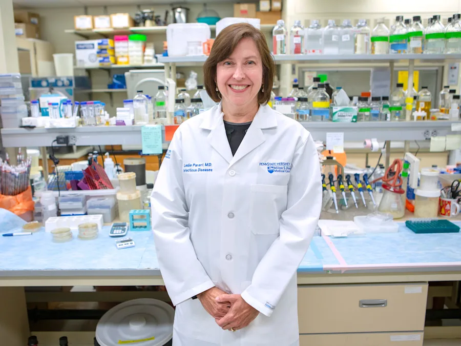 A photo of Dr. Leslie Parent posed in her Infectious Diseases lab at a workstation filled with bottles and equipment