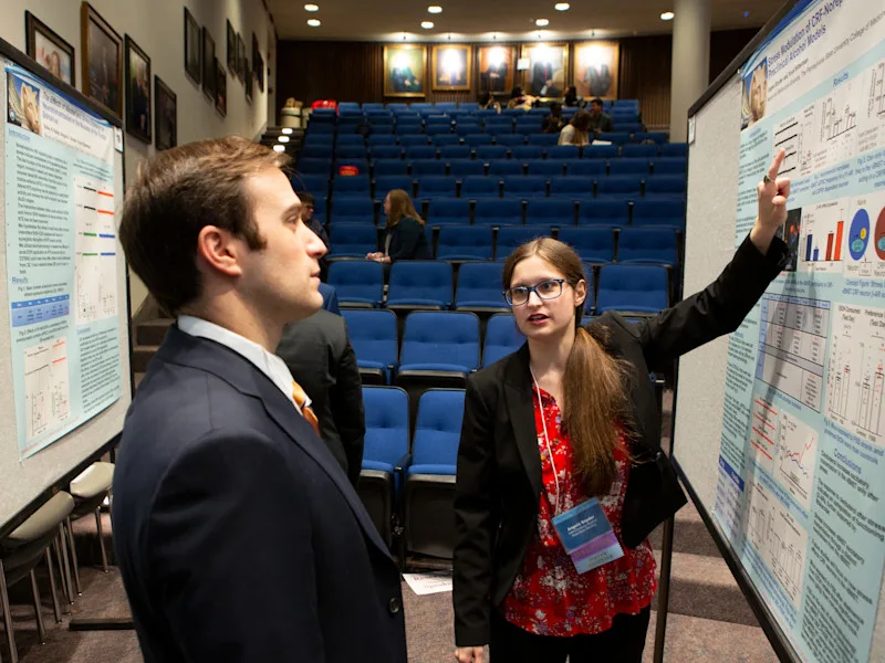 A woman points to a poster while discussing her addiction research.