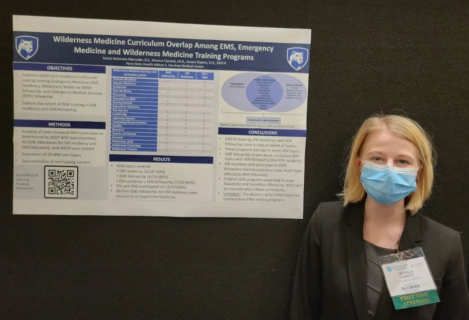 Dr. Monica Corsetti stands next to a presentation on Wilderness Medicine curriculum. 