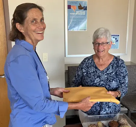 A woman holding something while another looks on, both smiling