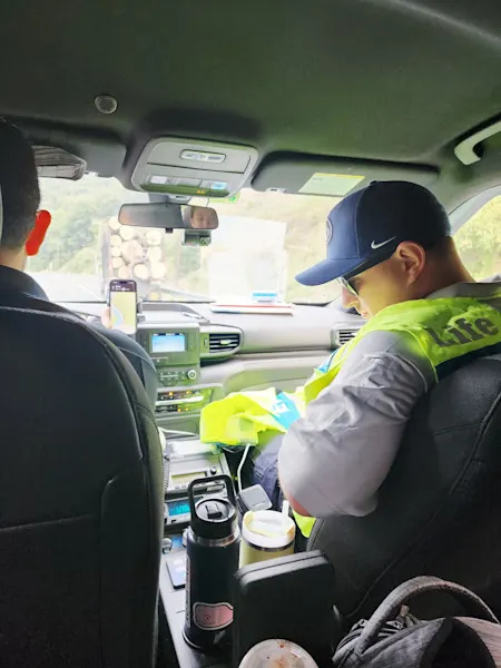 View from behind of two EMS fellows in the front seat of an emergency vehicle while on scene