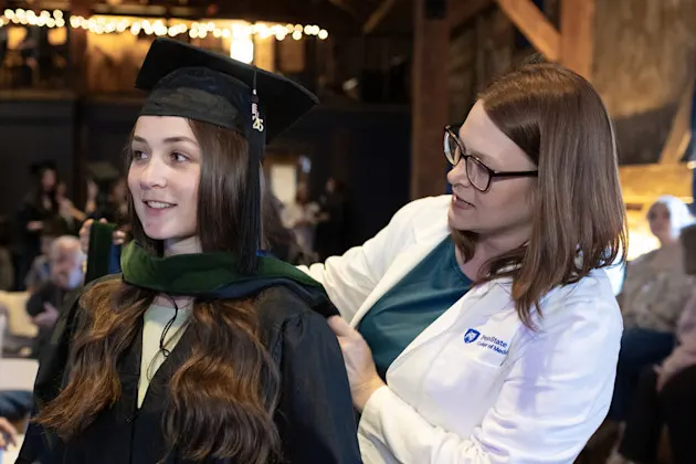 Kyla Brossoit is shown the hooding process from Larissa Whitney, DBA, MHS, Assistant Dean and PA Program Director