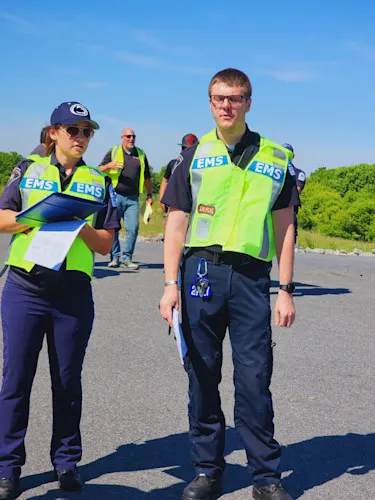 Two fellows in yellow vests with EMS during a drill; one holds a clipboard