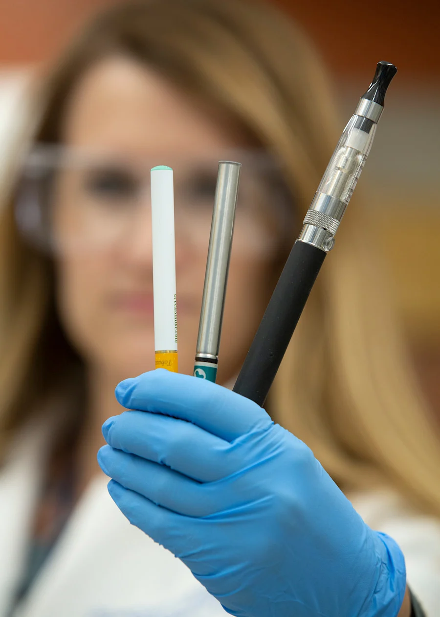 Scientists holds up three vaping and e-cigarette devices