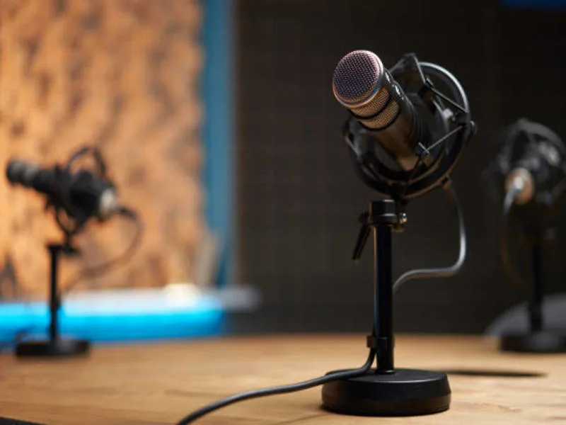 A podcast microphone sits on a desk in a recording studio.