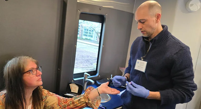 Dr. Michael McShane, wearing blue gloves, prepares to hand something to a woman who has her hand outstretched
