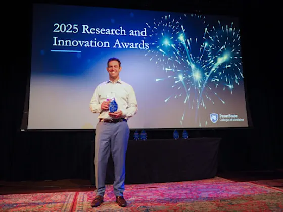Seth Pantanelli holds an award in front of a presentation slide stating 2025 Research and Innovation Awards