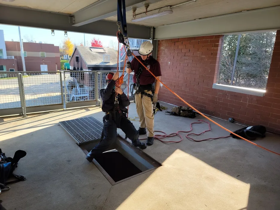 EMS fellows participate in a training exercise; one fellow is about to be lowered into a hole with a rope and pully system