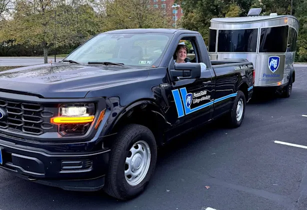 A woman drives a pickup hauling an Airstream trailer, both branded with Penn State College of Medicine, used for rural health