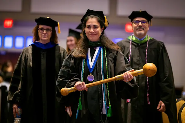 Dr. Emmanuelle Williams, flanked by two other leaders, leads the commencement processional holding the mace.