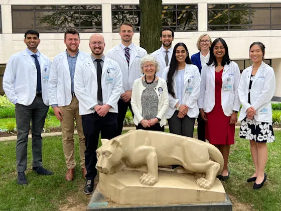 Group of 10 people, students and faculty behind the Nittany Lion statue in the College of Medicine courtyard