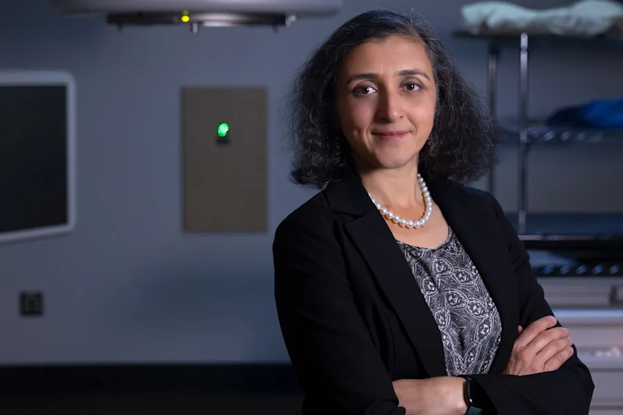 Radiation Oncologist Vinita Takiar poses in front of a linear accelerator 