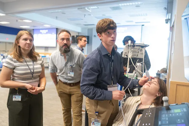 A medical student performs an ultrasound of a woman's eyeball while a student and faculty member watch
