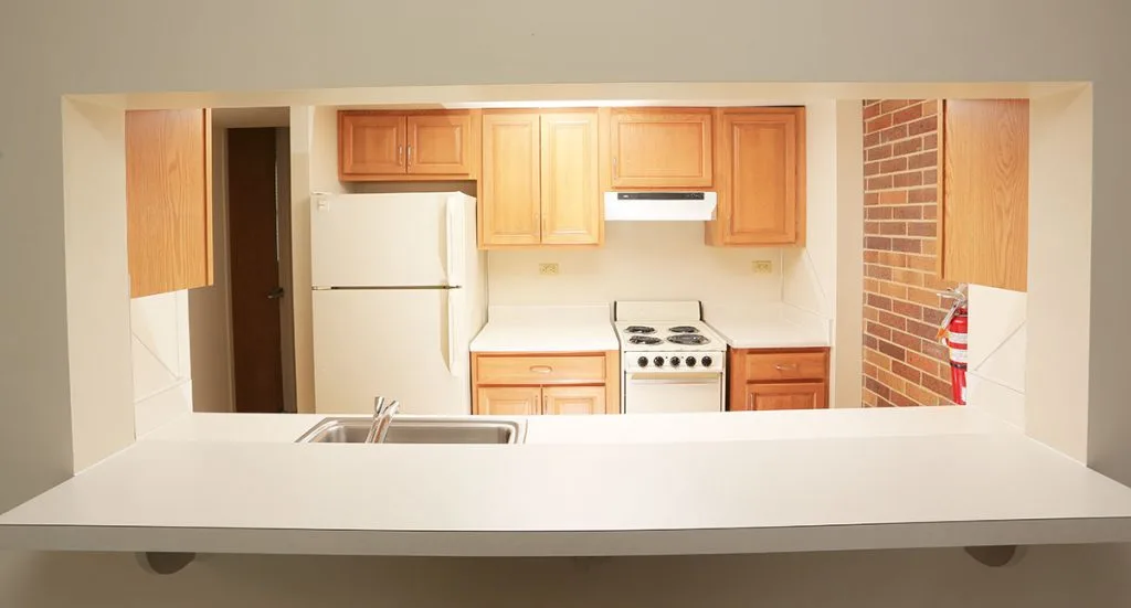 Galley kitchen at University Manor East shows a refrigerator, cabinets, stove and countertop.