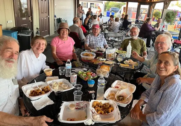 A group of seven people sit around a table with food in front of them