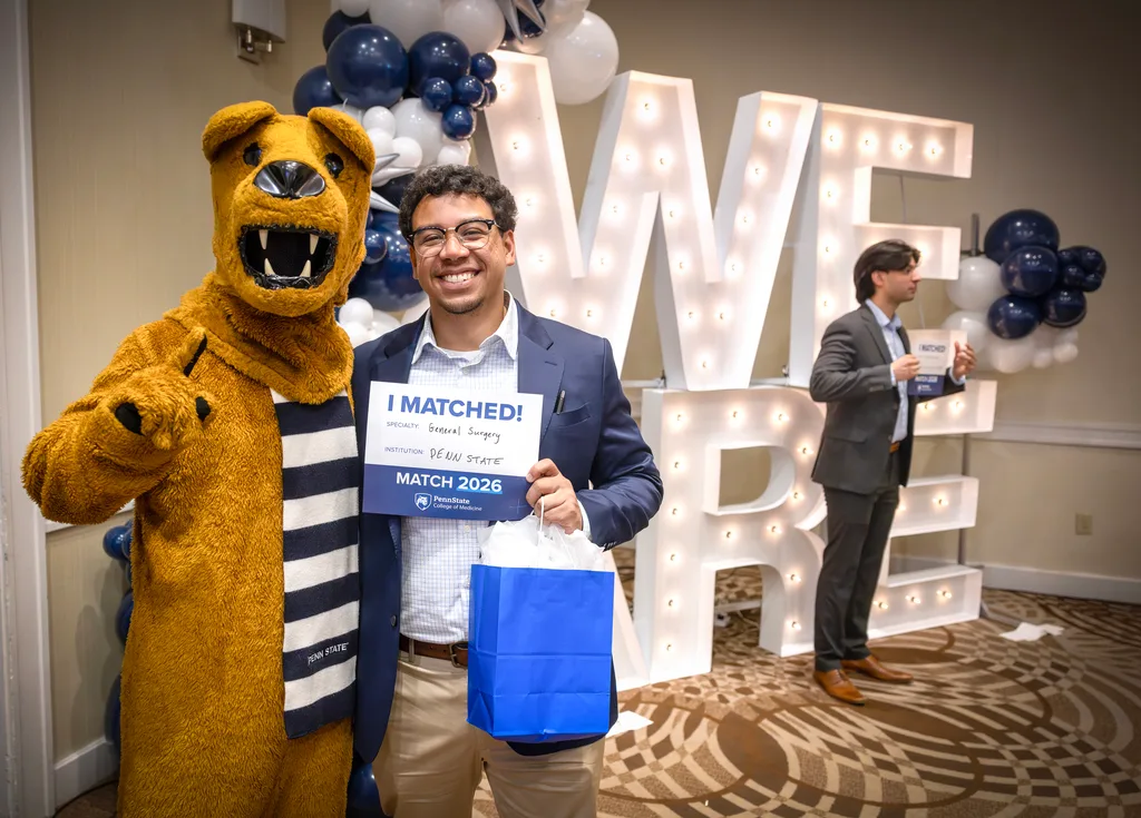 An MD student holds an 'I Matched!' sign while posing with the Nittany Lion