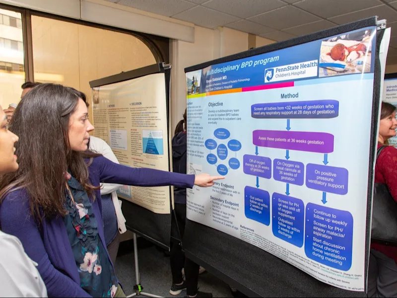A woman points to an academic poster project as part of a past Health Systems Science Academy cohort.