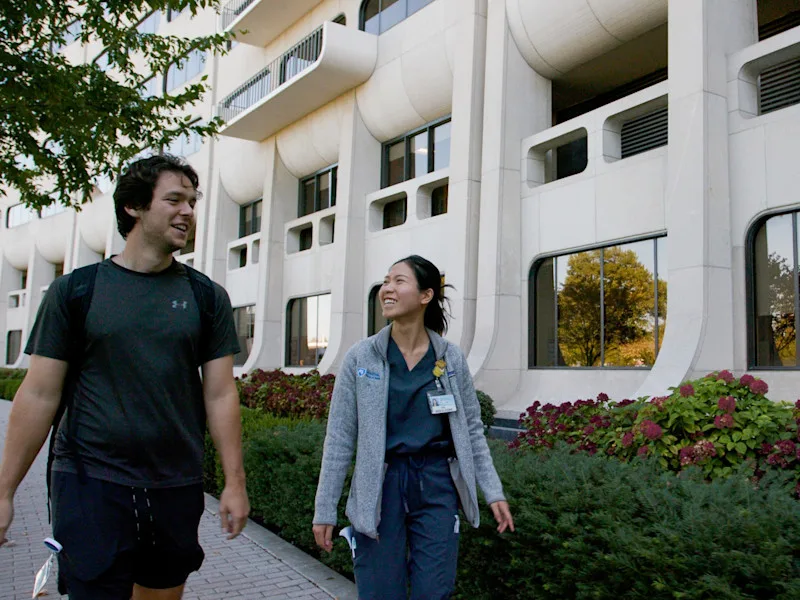 Medical students smiling and talking as they walk outside the crescent building at Penn State College of Medicine