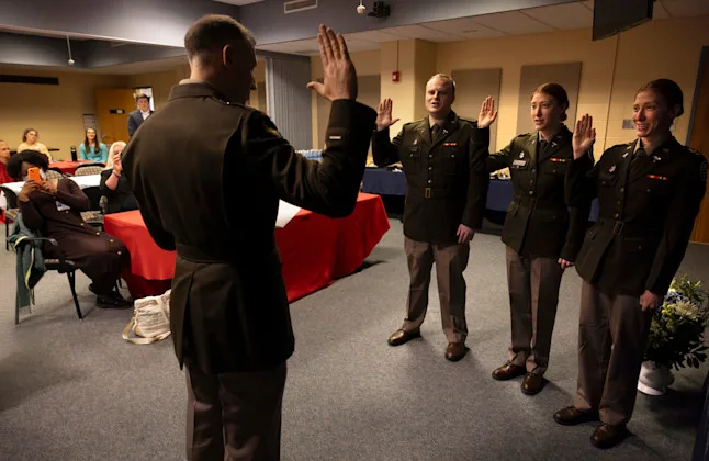 Three graduating medical students in military dress clothes raise their right hands to recite an oath