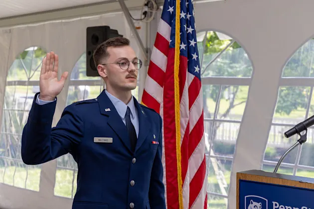 Captain William Mathias, USAF, raises his right hand and recites the Military Oath of Office with a U.S. flag next to him