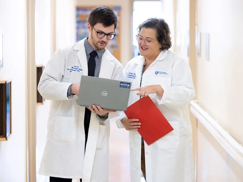 Micaiah Grien, left, and Heidi Runk, wearing white labcoats and looking at a computer at the Neuroscience Institute