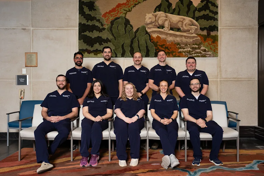 10 residents, 5 seated in front and 5 standing behind, in front of a wall with Penn State artwork