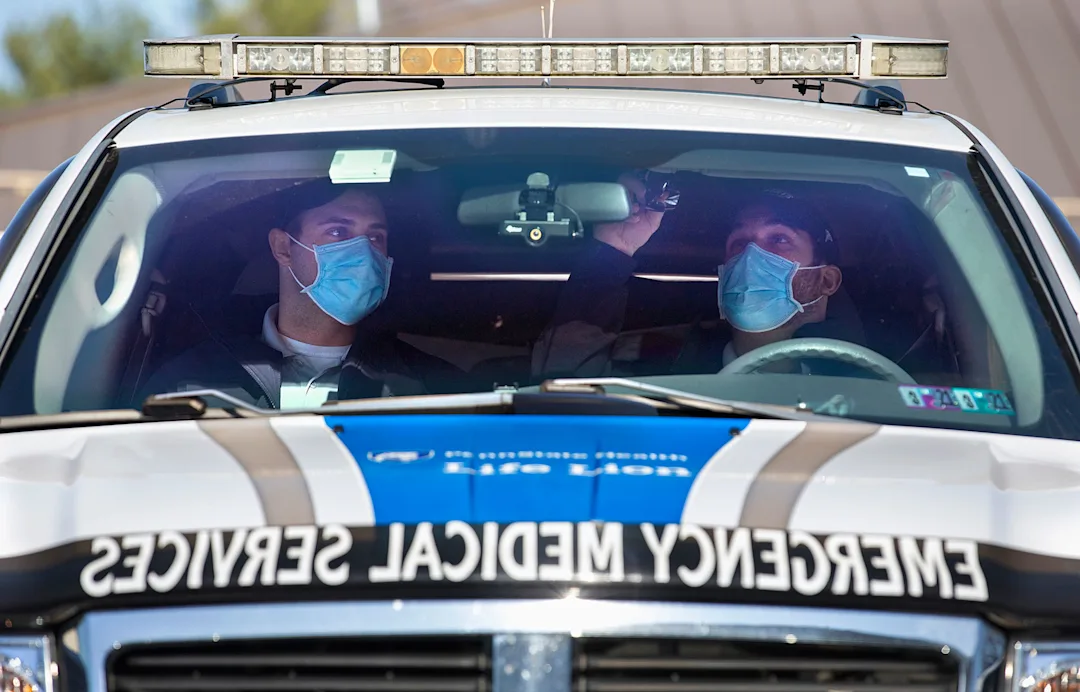 Penn State College of Medicine EMS Fellowship trainees, both wearing masks, are seen in the front seat of an EMS vehicle.